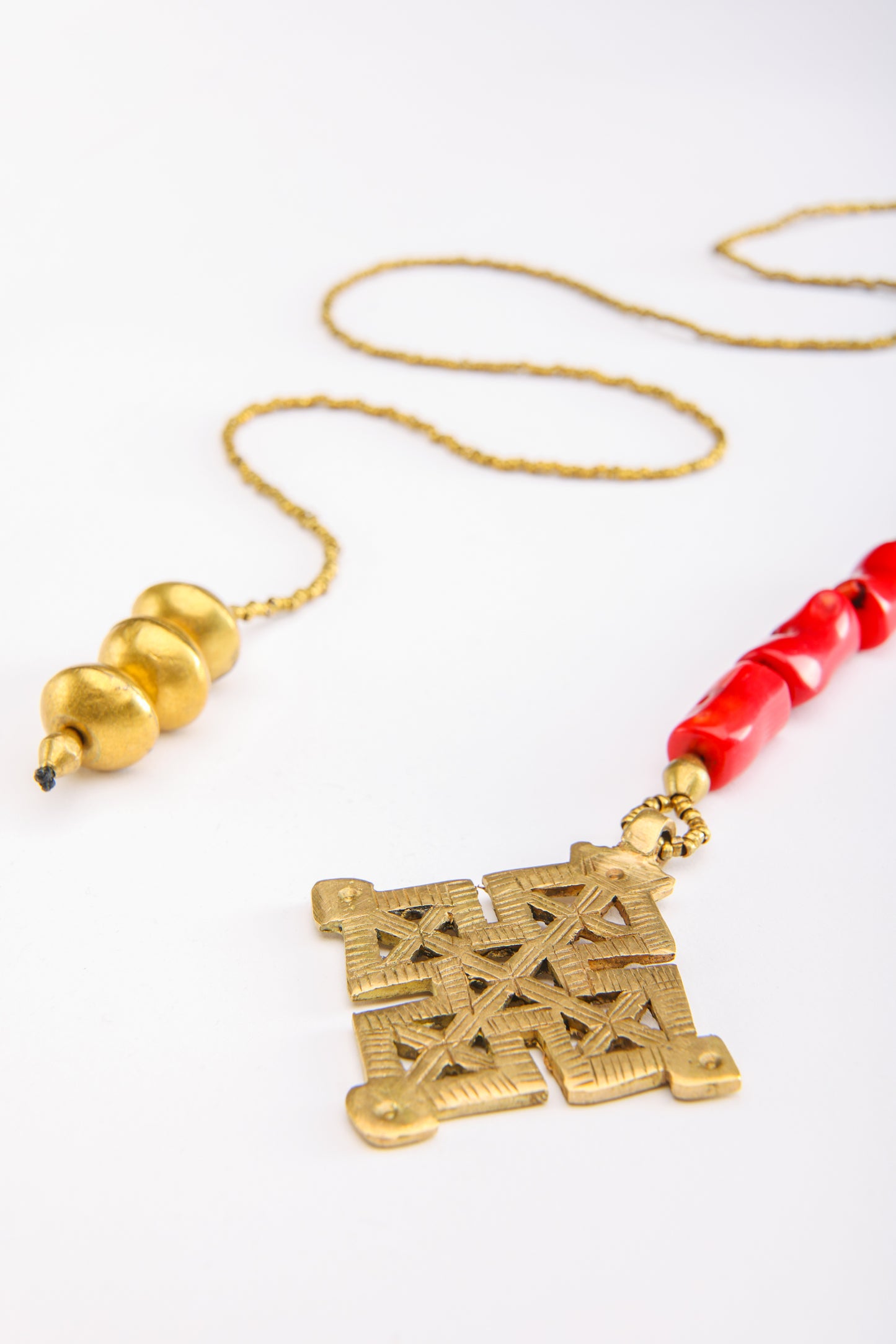Close-up of Ethiopian cross pendant with coral beads and weighted end on handcrafted necklace