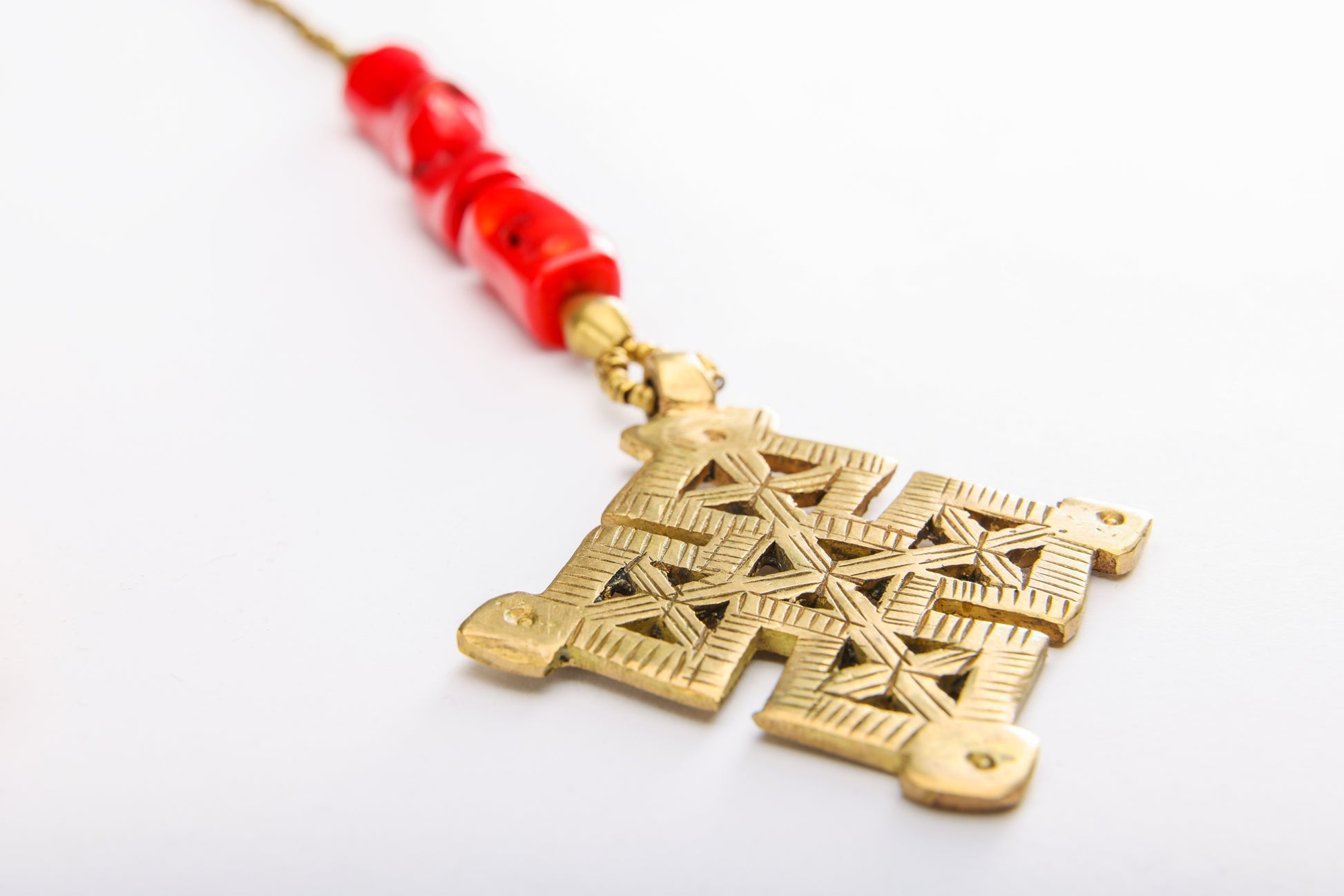 Close-up of Ethiopian cross pendant with vibrant coral beads on handcrafted brass necklace